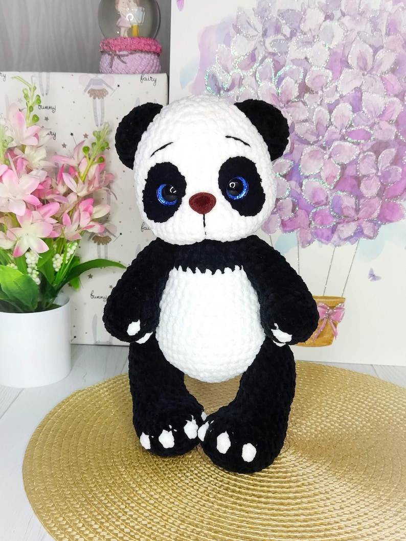 May include: A handcrafted panda bear soft toy in black and white. The panda has black ears, limbs, and a white body and head. It has blue eyes and a brown nose. The plush toy is designed to stand upright, a charming decorative item.