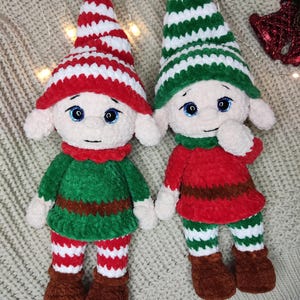 May include: Two handmade plush elf dolls. One elf wears a red and white striped hat, a green tunic, and red and white striped pants. The other elf wears a green and white striped hat, a red tunic, and green and white striped pants. Both have brown boots.