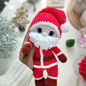 Puede incluir: Mu&ntilde;eco de Pap&aacute; Noel de felpa hecho a mano. El mu&ntilde;eco es principalmente rojo con ribetes blancos, barba blanca y gorro rojo con pomp&oacute;n blanco. Tiene ojos azules y guantes y botas marrones. El mu&ntilde;eco mide unos 15 cm de alto.