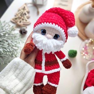 Puede incluir: Mu&ntilde;eco de Pap&aacute; Noel de felpa hecho a mano. El mu&ntilde;eco es principalmente rojo con ribetes blancos, barba blanca y gorro rojo con pomp&oacute;n blanco. Tiene ojos azules y zapatos y guantes marrones. Una decoraci&oacute;n navide&ntilde;a festiva.