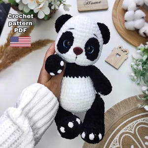 May include: A crocheted panda bear toy in black and white, with blue eyes and a brown nose. The panda is holding its paw up. The image includes the text "Crochet pattern PDF" and a US flag.