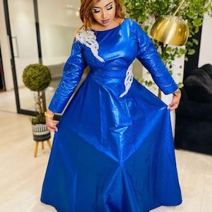 May include: A long, royal blue dress with long sleeves and a full skirt. The dress features white embroidered accents on the bodice and sleeves. The woman in the image is wearing a gold headband and bracelets.