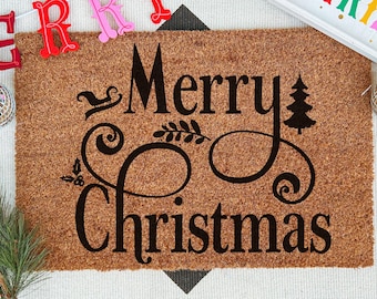 May include: A rectangular brown coir doormat featuring the black text Merry Christmas in a decorative script font. The design includes a small silhouette of a sleigh, a pine tree, and sprigs of holly. The mat has a coarse, natural fiber texture.