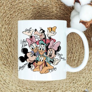 Puede incluir: Taza de cer&aacute;mica blanca con una colorida ilustraci&oacute;n de personajes de Disney, incluyendo Mickey Mouse, Minnie Mouse, Donald Duck, Daisy Duck, Goofy y Pluto. La taza tiene un asa curva y nombres de personajes.