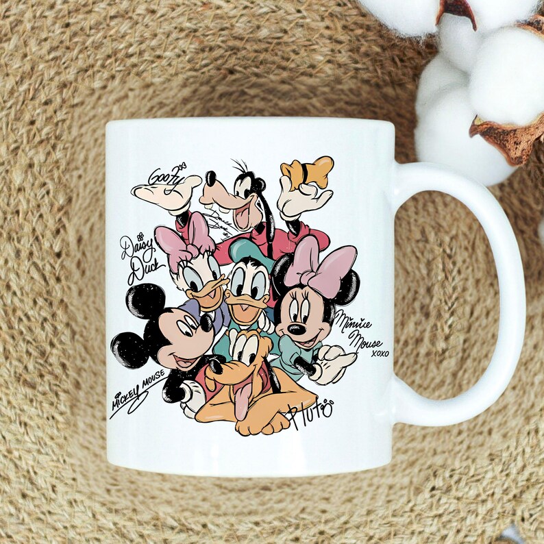 Puede incluir: Taza de cer&aacute;mica blanca con una colorida ilustraci&oacute;n de personajes de Disney, incluyendo Mickey Mouse, Minnie Mouse, Donald Duck, Daisy Duck, Goofy y Pluto. La taza tiene un asa curva y nombres de personajes.