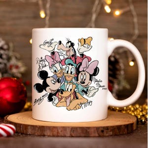 Puede incluir: Taza de cer&aacute;mica blanca con una colorida ilustraci&oacute;n de personajes de Disney, incluyendo Mickey Mouse, Minnie Mouse, Donald Duck, Daisy Duck, Goofy y Pluto. La taza tiene un asa grande y est&aacute; sobre una superficie de madera.