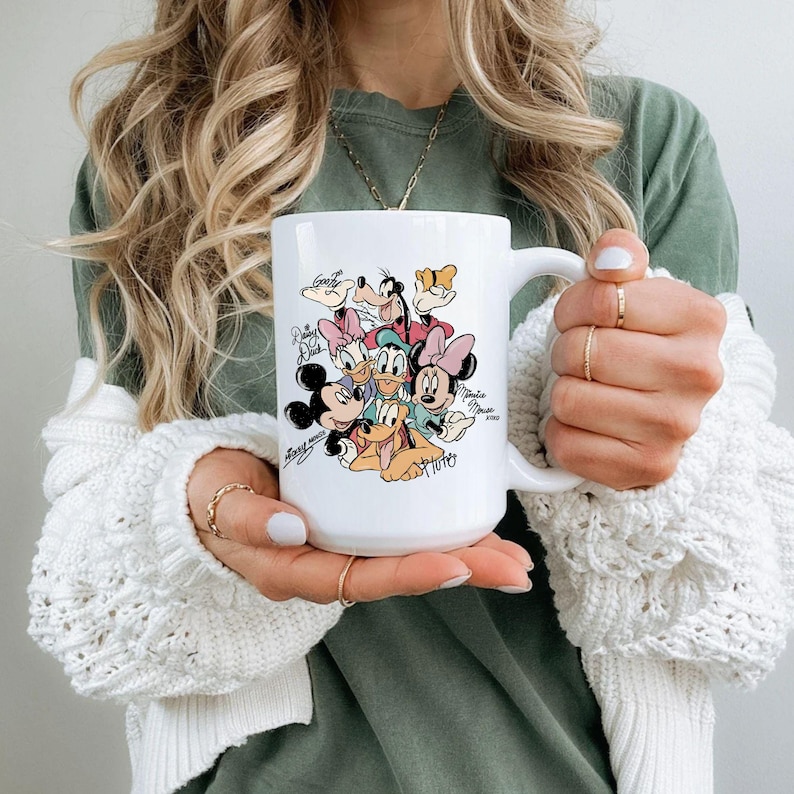 Puede incluir: Taza de cer&aacute;mica blanca con una colorida ilustraci&oacute;n de personajes de Disney, incluyendo Mickey Mouse, Minnie Mouse, Donald Duck y Pluto. La taza tiene un asa grande y firmas de personajes.