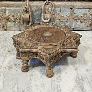 Könnte beinhalten: Ein kleiner, aufwendig geschnitzter Holztisch mit achtzackigem Sternmuster. Der Tisch hat kurze, abgerundete Beine und ist aus dunkelbraunem Holz gefertigt. Der Hintergrund zeigt eine verwitterte Holztür mit Metallbeschlägen.
