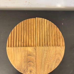 May include: A circular wooden object divided into two equal halves. Each half features a smooth, flat bottom section and a top section with vertical, parallel grooves carved into the surface. The wood displays a natural light brown grain pattern.
