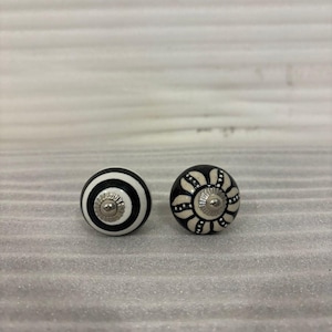 May include: Two decorative ceramic cabinet knobs. One knob features a black and white striped design, while the other has a black background with a white floral pattern. Both knobs have a silver metal base.