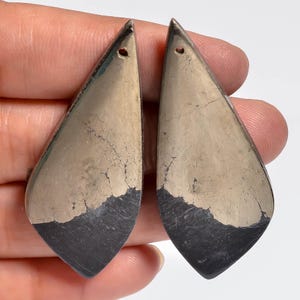 May include: Two teardrop-shaped pyrite pendants with a polished metallic gold finish on the upper sections and a dark, matte charcoal grey base. Each piece features a small drilled hole at the top point for suspension, showcasing natural mineral textures.