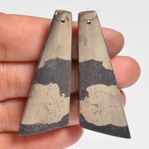 May include: Two elongated, trapezoidal-shaped pendants made of metallic pyrite with a distinct mottled pattern of dark grey and shimmering brassy gold tones. Each piece features a small, circular drilled hole at the top for suspension.