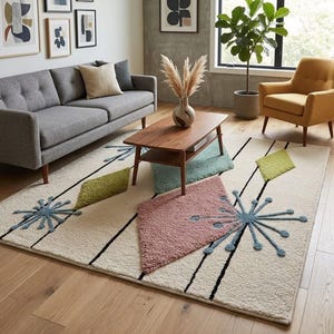 Op de afbeelding: Een crèmekleurig vloerkleed met een modern design uit het midden van de eeuw. Het vloerkleed heeft zwarte lijnen, geometrische vormen in groen, roze en blauw en stervormige patronen. Het vloerkleed ligt in een woonkamer met een grijze bank en een houten salontafel.