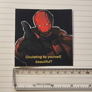 May include: Square sticker featuring a comic book style illustration of a character in a red helmet and costume, pointing. The text "Ovulating by yourself, beautiful?" is in yellow. The sticker is approximately 3 inches wide.