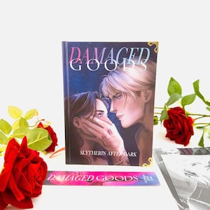 May include: A book titled "DAMAGED GOODS" with a cover illustration of two people. A matching bookmark and red roses are also present. The text "SLYTHERIN AFTER DARK" is visible on the book's cover.