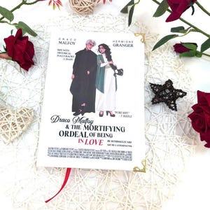 May include: A book cover with Draco Malfoy and Hermione Granger illustrated on it. The title is "Draco Malfoy & The Mortifying Ordeal of Being in Love." The cover art shows the characters in a romantic pose. The book has gold corner protectors and a red ribbon bookmark.
