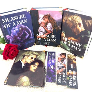 Op de afbeelding: Een verzameling boeken en bladwijzers met de titel "Measure of a Man". De boeken zijn gelabeld als Vol. 1, Vol. 2 en Vol. 3. De covers bevatten illustraties van mensen. Bladwijzers tonen ook de titel.