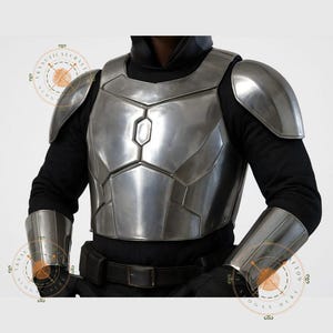 Op de afbeelding: Een zilverkleurige borst- en schouderpantser set met bijpassende armbeschermers. Het pantser wordt gedragen over een zwart shirt met lange mouwen en vastgezet met een zwarte riem. Het ontwerp doet denken aan sciencefiction- of fantasiekostuums.