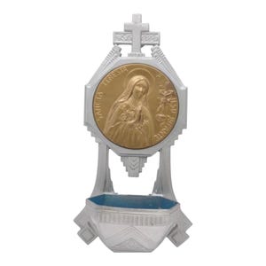 Peut inclure: Un bénitier argenté avec un médaillon doré représentant une figure religieuse et l'inscription "SANCTA TERESIA JESU INFANTE". Le bénitier comporte une croix et un petit bassin à intérieur bleu.