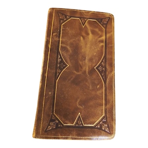 Peut inclure: Un livre rectangulaire en cuir marron de style ancien. La couverture présente une bordure dorée décorative avec des motifs d'angle ornés. Le cuir a un aspect texturé et le livre est légèrement incliné.