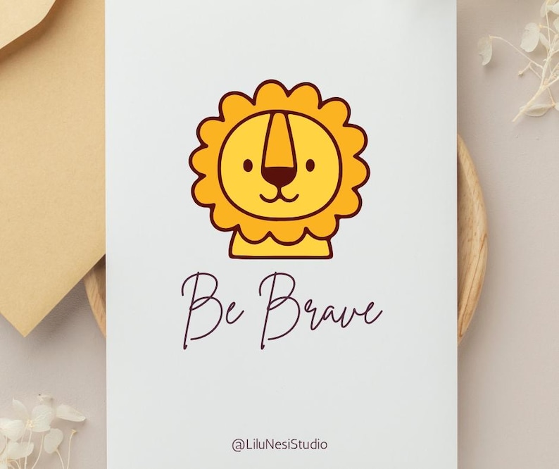 May include: A white card with a cartoon lion illustration in yellow and brown. The text "Be Brave" is written in a cursive font below the lion. The artist's name, "@LiluNesiStudio", is at the bottom.