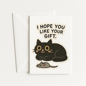 May include: A white greeting card featuring a black cat illustration and the text "I HOPE YOU LIKE YOUR GIFT." The cat has yellow eyes and is next to a grey mouse. A white envelope is behind the card.