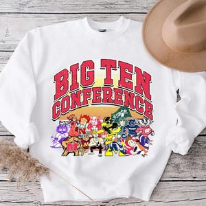 May include: White sweatshirt featuring the text "BIG TEN CONFERENCE" in red and yellow, with a distressed effect. Below the text are cartoon mascots of various college teams. A brown hat rests on the right side of the sweatshirt.