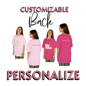 以下が含まれることがあります： 「Girl Boss」と「Troop 2002」の文字がプリントされたピンクとフクシアのTシャツ。画像には、「CUSTOMIZABLE Back」と「PERSONALIZE」の文字もピンクと黒のテキストで含まれています。