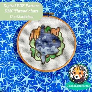 May include: A cross-stitch pattern in a wooden hoop features a blue and white design surrounded by orange and green accents. The text "Digital PDF Pattern DMC Thread chart 37 x 42 stitches" is visible. The background is a blue fabric with white star patterns.
