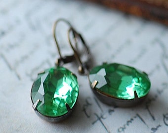 May include: A pair of green gemstone earrings with bronze-colored hooks. The gemstones are oval-shaped and have a faceted cut.