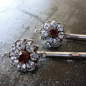 May include: Two silver hair pins with a red rhinestone and clear rhinestones in a flower design.