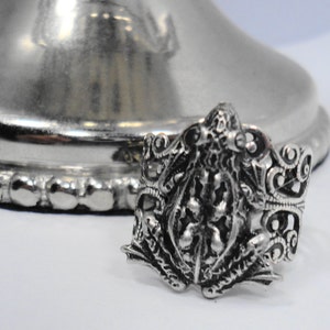 May include: A silver ring with a detailed design of a frog. The ring is ornate and has a filigree design.