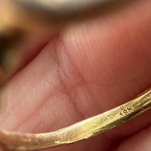Peut inclure: Gros plan sur une bague en or avec un poin&ccedil;on 18K. Le corps de la bague est de couleur or chaud et la surface pr&eacute;sente une l&eacute;g&egrave;re usure. La bague est tenue par une personne, l'accent &eacute;tant mis sur les d&eacute;tails de la bague.