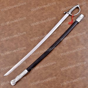 May include: A silver saber with a curved blade and a decorative handle, resting beside its black scabbard. The scabbard has silver accents. The blade is approximately 36 inches long. The image is on a brown background, with the text "WildKnivesStore" repeated.