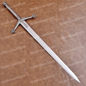 May include: A silver-toned metal sword featuring a long, double-edged blade with a central fuller. The hilt includes a crossguard with four-lobed terminals and a textured, patterned grip, topped with a spherical pommel. The text WildKnivesStore is visible.