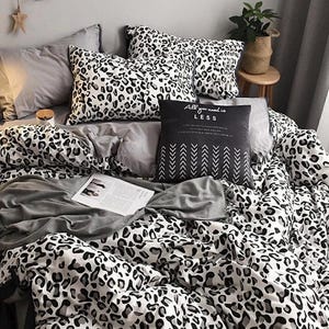Könnte beinhalten: Ein Bett mit einer Bettdecke, Kissen und Bettwäsche mit Leopardenmuster in Schwarz und Weiß. Das Bett hat auch eine graue Decke und ein schwarzes Kissen mit dem Text "All you need is LESS". Eine Zeitschrift ist auf dem Bett geöffnet.