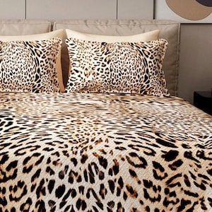 Puede incluir: Juego de cama con estampado de leopardo. El juego incluye dos almohadas y una colcha, todas con un patr&oacute;n de manchas beige y marr&oacute;n. Las almohadas est&aacute;n colocadas sobre un cabecero beige. La ropa de cama tiene una paleta de colores neutros.