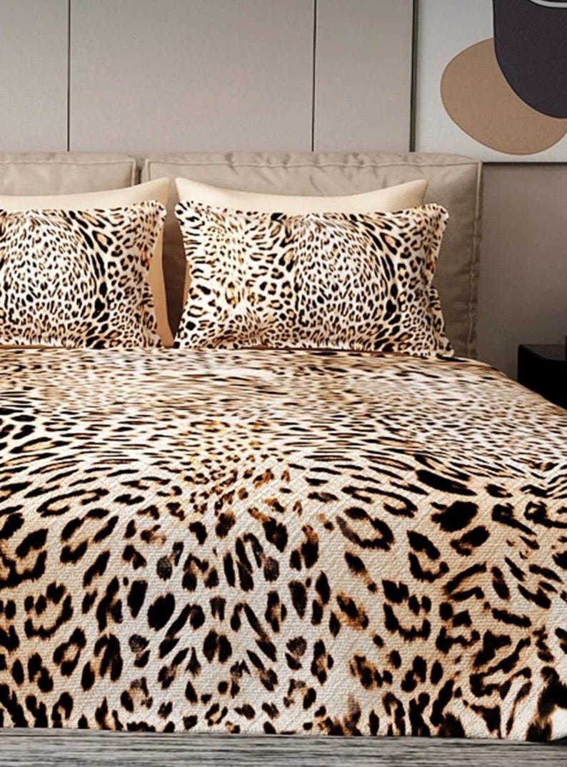 Puede incluir: Juego de cama con estampado de leopardo. El juego incluye dos almohadas y una colcha, todas con un patr&oacute;n de manchas beige y marr&oacute;n. Las almohadas est&aacute;n colocadas sobre un cabecero beige. La ropa de cama tiene una paleta de colores neutros.
