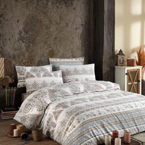 Puede incluir: Juego de cama blanco con estampado de elefantes y geométrico. La funda nórdica y las fundas de almohada presentan un diseño en tonos blancos, marrones y azules. La ropa de cama se muestra en una cama en una habitación de estilo rústico y bohemio.