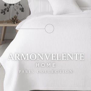 May include: A white bed set with a ribbed texture, including a duvet cover, pillows, and pillowcases. The image shows a close-up of the fabric's weave and the text "ARMONVELENTE HOME PARIS COLLECTION."