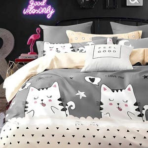 May include: A grey and white cat-themed bedding set with a playful design. The duvet cover features large cartoon cats, stars, and the phrase "I Love You." A white pillow displays "Feel Good."