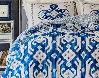 May include: A bed with a white headboard and bedding featuring a blue and white ikat pattern. The duvet cover and pillowcases display a repeating geometric design in shades of blue and white. The overall theme is a modern, bohemian style.