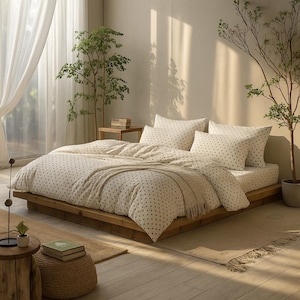Può includere: Una camera da letto con un letto basso in legno, coperto da un piumino e federe color crema con piccoli pois scuri. Una coperta beige è sul letto. La stanza è illuminata dalla luce naturale e ha piante decorative.