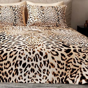 Puede incluir: Juego de cama con estampado de leopardo. El conjunto incluye una funda n&oacute;rdica y dos fundas de almohada. El dise&ntilde;o presenta manchas marrones y negras sobre un fondo beige, creando una est&eacute;tica salvaje y ex&oacute;tica. La ropa de cama est&aacute; colocada sobre una cama.