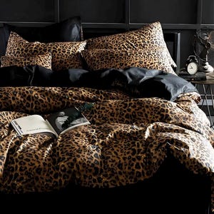 May include: A bed with a leopard print comforter, pillows, and sheets. The bedding has a brown and black spotted pattern. Black pillows and sheets are also visible. An open book is on the bed.