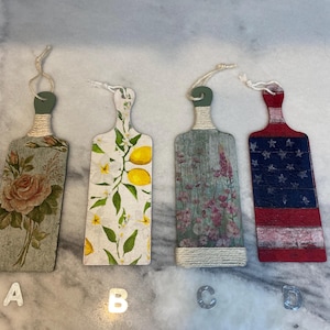 May include: Four decorative wooden cutting boards with various designs. One features roses, another lemons, a third pink flowers, and the last a US flag. Each board has a twine-wrapped handle and a string for hanging.