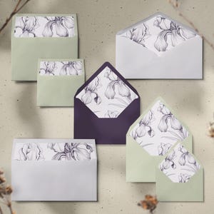 May include: An assortment of envelopes in various sizes and colors, including white, sage green, and deep purple. Each envelope features a floral iris design on the interior lining. The envelopes are arranged on a neutral background.