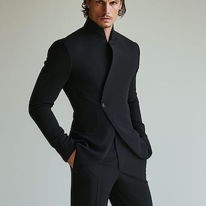 May include: A black suit with a unique asymmetrical design. The jacket features a high, mandarin-style collar and a single-button closure. The suit is made of a textured fabric, and the pants are straight-legged.