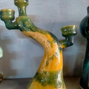 Peut inclure: Un chandelier en céramique avec trois bougeoirs. Le chandelier a un design en forme d'arbre avec des couleurs jaune, vert et marron. La base est jaune, passant au vert et au marron sur la partie supérieure.