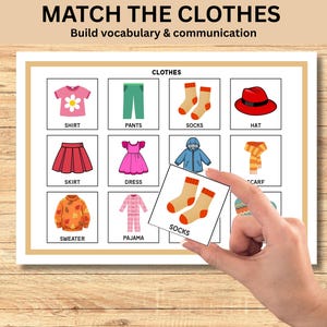 May include: Educational game with clothing illustrations. The game includes a grid of clothing items such as a shirt, pants, socks, hat, skirt, dress, sweater, pajama, and scarf. A hand holds a card with socks, matching the image on the game board. Text reads "MATCH THE CLOTHES" and "Build vocabulary & communication."